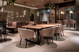 Moderne vergaderruimte met houten tafel, beige stoelen, bruine lounge bank, hangende verlichting en grijs-bruine wandafwerkin