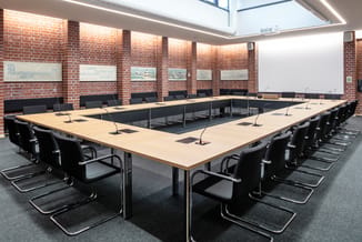 Moderne vergaderzaal met U-vormige houten tafel, zwarte kantelstoelen, bakstenen wanden, skylight, witte whiteboard en microf