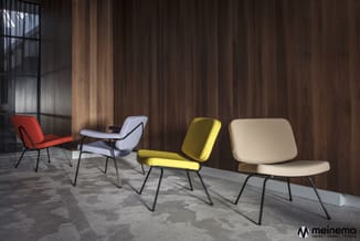 Vier lounge chairs in verschillende kleuren (rood, wit, geel, beige) met metalen poten in moderne kantoorruimte met houten wa