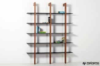 Modulair wandkastensysteem met drie houten verticale elementen en zes zwarte horizontale planken, gevuld met boeken, tegen wi