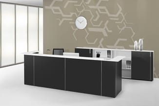 Moderne receptiebalie met zwarte voorkant en wit blad, aangevuld met witte open kasten, in een kantoor met beige geometrisch