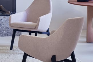 Twee beige stoelen met zwarte houten poten in een woonruimte, op een tapijt bij een roze tafel met decoratieve objecten.