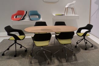 Moderne vergaderruimte met ovale houten tafel, zwarte stoelen met gele zitting, wit plateau met kleurrijke designstoelen op a