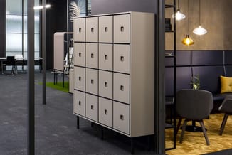Moderne locker kast met 16 compartimenten in beige en zwart, met kleine handgrepen, in open kantoorruimte met zithoek.
