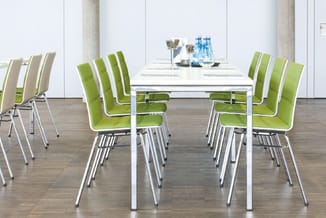 Moderne vergadertafel met witte frame en groen-witte bezoekersstoelen met aluminium poten in kantoorruimte met betonnen zuile