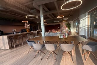 Moderne kantoorruimte met houten vergadertafel, grijze stoelen met houten poten, bar links, circulaire neonverlichting plafon