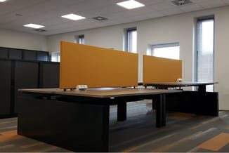 Moderne kantoorruimte met grote zwarte vergadertafel, houten blad, gele akoestische schermen en ramen met lamellen.