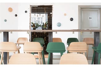 Modern kantoor met houten en groene stoelen aan tafel, glazen deur met planten, wanddecoratie met ronde elementen en deurtoga