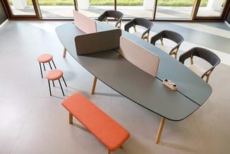 Vergadertafel met grijsblauwe tafelblad, roze en bruine scheidingspanelen, houten poten. Omgeven door zwarte stoelen, oranje
