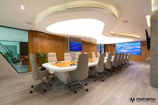 Moderne vergaderruimte met ovale wit-houten tafel, beige bureaustoel, houten wandbekleding, rond plafondlicht en schermen aan