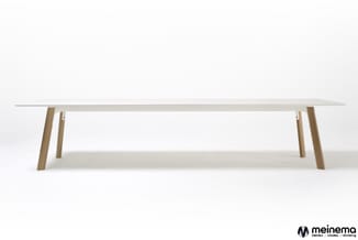 Lange witte vergadertafel met natuurhouten poten op een witte achtergrond.
