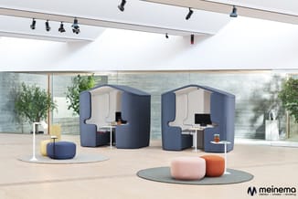 Modern kantoorinterieur met twee blauwe akoestische belcellen, roze en oranje poefjes, gele zitpuf en tafeljes op houten vloe