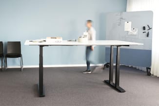 Elektrisch verstelbaar bureau met wit blad en zwart onderstel in moderne kantoorruimte met blauwe wand en akoestische scherme