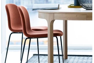 Twee roestbruine stoelen met gewelfde rugleuning en zwarte metalen poten bij een licht houten bureau in een kantoorruimte met