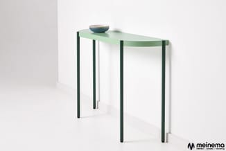 Groene halfronde console tafel met lichte blad en donkergroene poten, gesteld tegen witte wand met gestapelde borden erop.