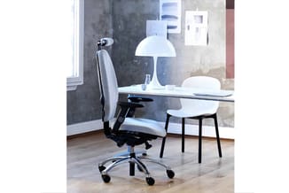 Modern kantoor met witte ergonomische bureaustoel, glazen bureau, witte paddenstoelvormige lamp en witte bezoekersstoel tegen