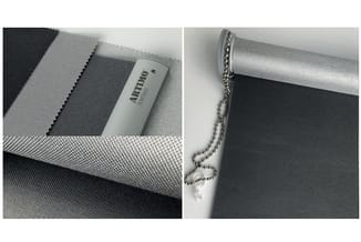 Rolgordijn in grijs en zwart met "Albinno" branding op rol, detail van stof textuur en bevestigingsmechanisme met ketting.