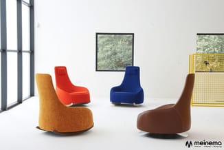 Vier gekleurde loungefauteuils in moderne vorm met ronde basis in oranje, rood, donkerblauw en bruin, geplaatst in minimalist