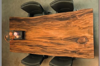 Houten vergadertafel met organische rand en zwarte bureaustoelen, bovenaanzicht met stopcontact zichtbaar.