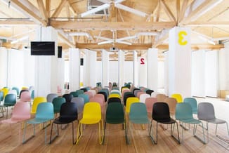 Moderne conferentieruimte met gekleurde kunststofschelpstoelen (roze, geel, turquoise, grijs, zwart, groen) op metalen frames