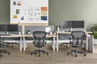 Modern kantoor met twee houten bureaus, grijze akoestische schermen, zwarte ergonomische bureaustoelen, monitoren en presenta