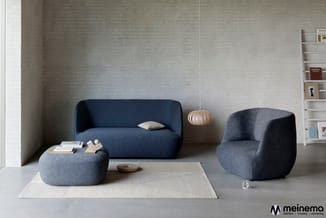 Moderne lounge met donkerblauwe sofa, twee grijze fauteuils, grijze poef, beige vloerkleed en witte wandkasten tegen lichtgri