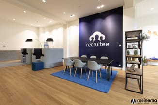 Recruitee kantoor met donkerblauwe accent-wand, zwarte vergadertafel met grijze stoelen op blauwe vloerkleed, lounge-hoek met