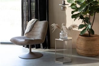 Grijze draaibare fauteuil met voetsteun naast glazen bijzettafel en wicker plantenbak in moderne kantoorruimte.