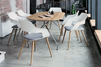 Ronde houten vergadertafel met vier witte stoelen met grijze zitussen en houten poten, in moderne kantoorruimte met betonvloe