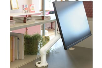 Monitor op verstelbare witte monitorarm op kantoorbureau met boeken, plant en raam op achtergrond.