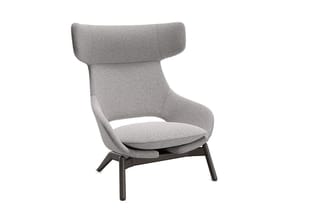 Grijze fauteuil met hoge gebogen rugleuning, zitplaats met kussen en donkerbruin houten onderstel op vier poten.