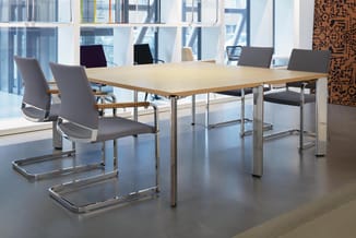 Moderne vergadertafel met licht hout blad en stalen onderstel, omgeven door grijze kantoorstoel met chroom frame in licht kan