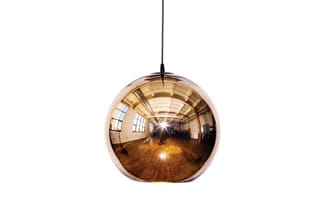 Hangende glazen bolpendel met spiegelend bronzen oppervlak, zwart ophangsnoer, boven houten vloer in industrieel ruimte.