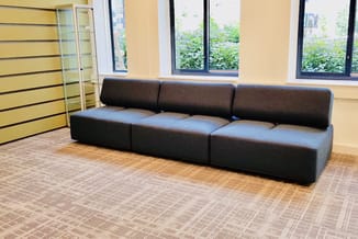 Modulaire zwarte zitbank met vier elementen in moderne kantoorruimte met gele wanden en grote ramen.