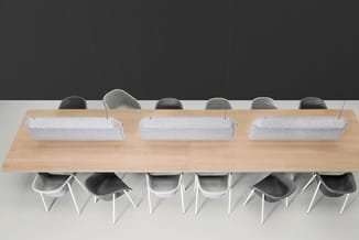 Lange houten vergadertafel met grijze akoestische schermen en grijze stoelen met witte poten tegen donkergrijze wand.