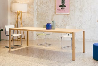 Houten vergadertafel met naturel blad, omgeven door witte stoelen met metalen frame in minimalistische kantoorruimte met beto