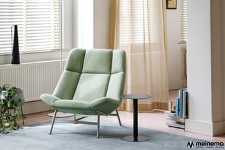 Groene gestoffeerde fauteuil met gequilte rugleuning en metalen poten in een lichte kantoorruimte met raam, zwart bijzettafel