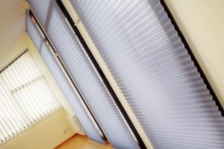 Verticale lamellen in wit en grijs aan plafond in gele ruimte met houten vloer