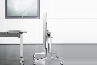 Mobiele displaystandaard op wielen in wit metaal met zwart scherm, in modern kantoorinterieur met whiteboard en tafel.