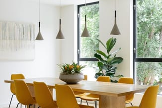 Moderne vergaderruimte met houten tafel, gele stoelen, hanglampen in grijs, potplanten en grote ramen met uitzicht op groen.