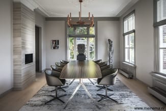 Moderne vergaderruimte met ovale houten tafel, zwarte draaistoelen, koperen hanglamp, grote ramen en kunstobjecten aan de wan