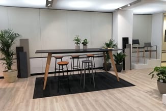 Moderne kantoorruimte met zwarte houten vergadertafel op houten poten, barkrukken, zwart tapijt, potplanten en grijze wandpan