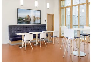 Moderne kantoorruimte met donkerblauwe U-vormige zitbank, witte barkrukken, houten tafels, houten ramen en TV aan muur.