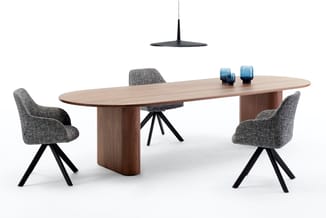 Ovale houten vergadertafel met bruine houten voet, vier grijze stoelen met zwarte poten, zwarte hanglamp en blauwe decoratiev