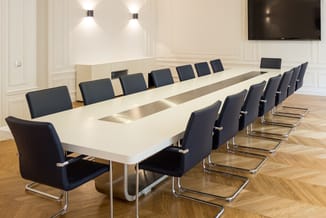 Moderne vergaderruimte met witte vergadertafel, zwarte kantooorstoelen met chromen frame en houten vloer.