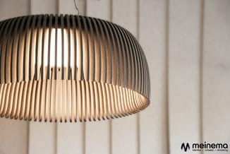 Hangende lamp met geribde dome-vormige kap in grijs en wit, verlicht tegen witte verticale wandpanelen.