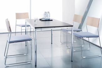 Moderne vergadertafel met zwart blad en chromen onderstel, omgeven door vier stapelbare stoelen met beige rugleuning en blauw