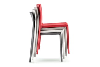 Gestapelde kunststof stoelen in rood, grijs, wit en zwart tegen witte achtergrond.