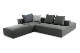 Grijze hoekbank met losse zittingselementen, vier decoratieve kussens in grijs en donkerblauw, modulair design.