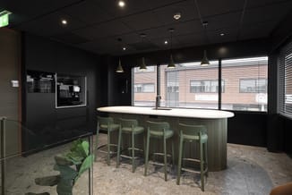 Moderne pantry met zwart gelakte kastenwand, wit werkblad, groen geribbelde fronten, vier groene barkrukken, hangende metalen